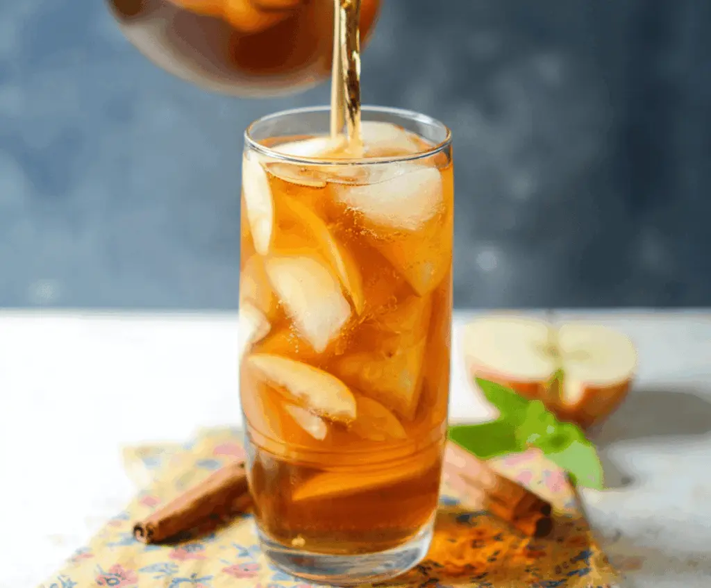 Refreshing glass of Apple Butter Iced Tea garnished with apple slices and mint leaves on a summer table.