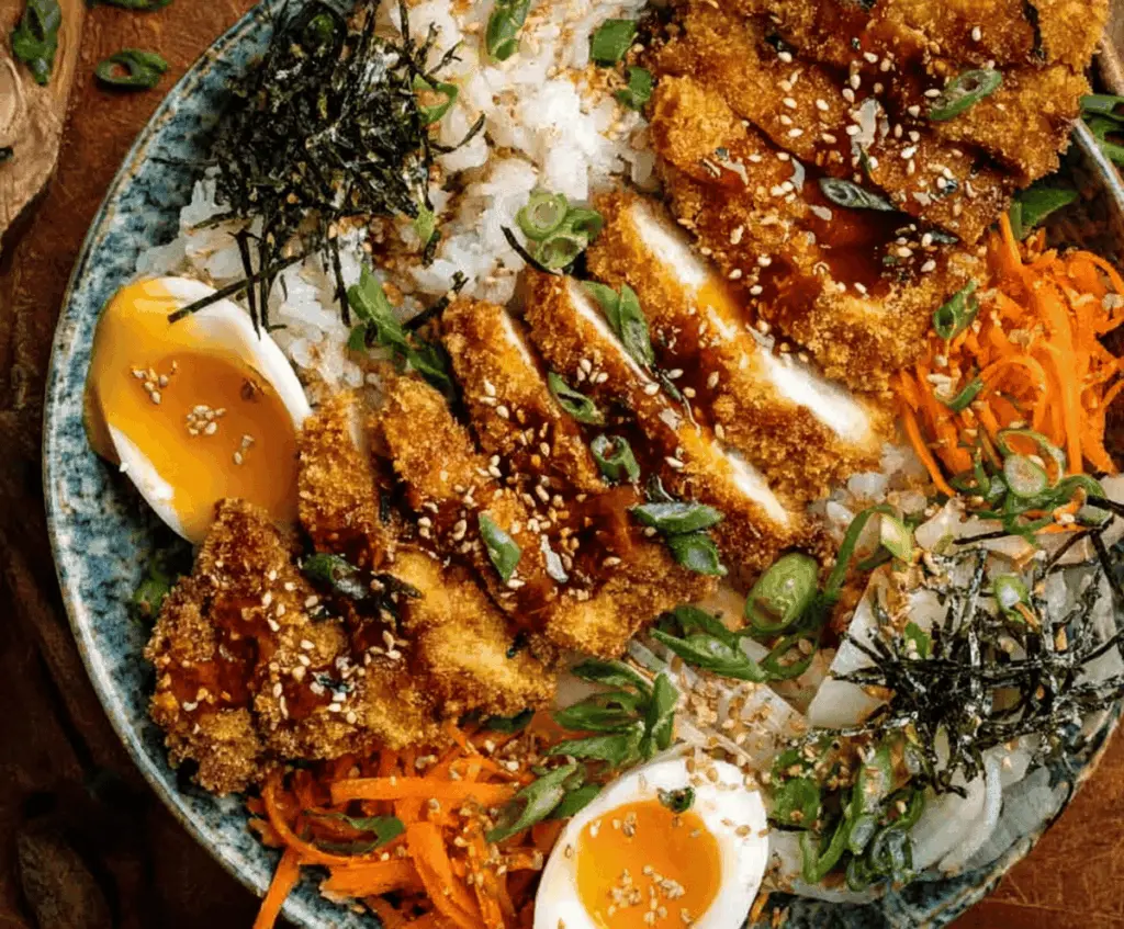 Delicious Japanese Katsu Bowls featuring crispy breaded pork cutlets, steamed rice, fresh vegetables, and savory sauce on a stylish plate