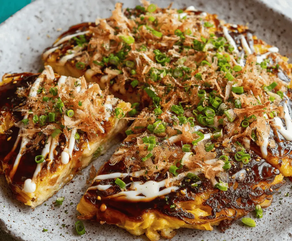 Delicious homemade Okonomiyaki Japanese savory pancake topped with mayonnaise, bonito flakes, and okonomiyaki sauce, served on a plate