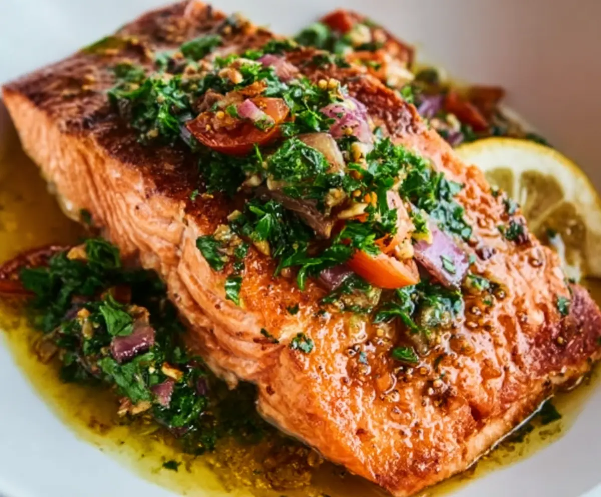 Delicious salmon fillet topped with vibrant sizzled nut salsa on a white plate.